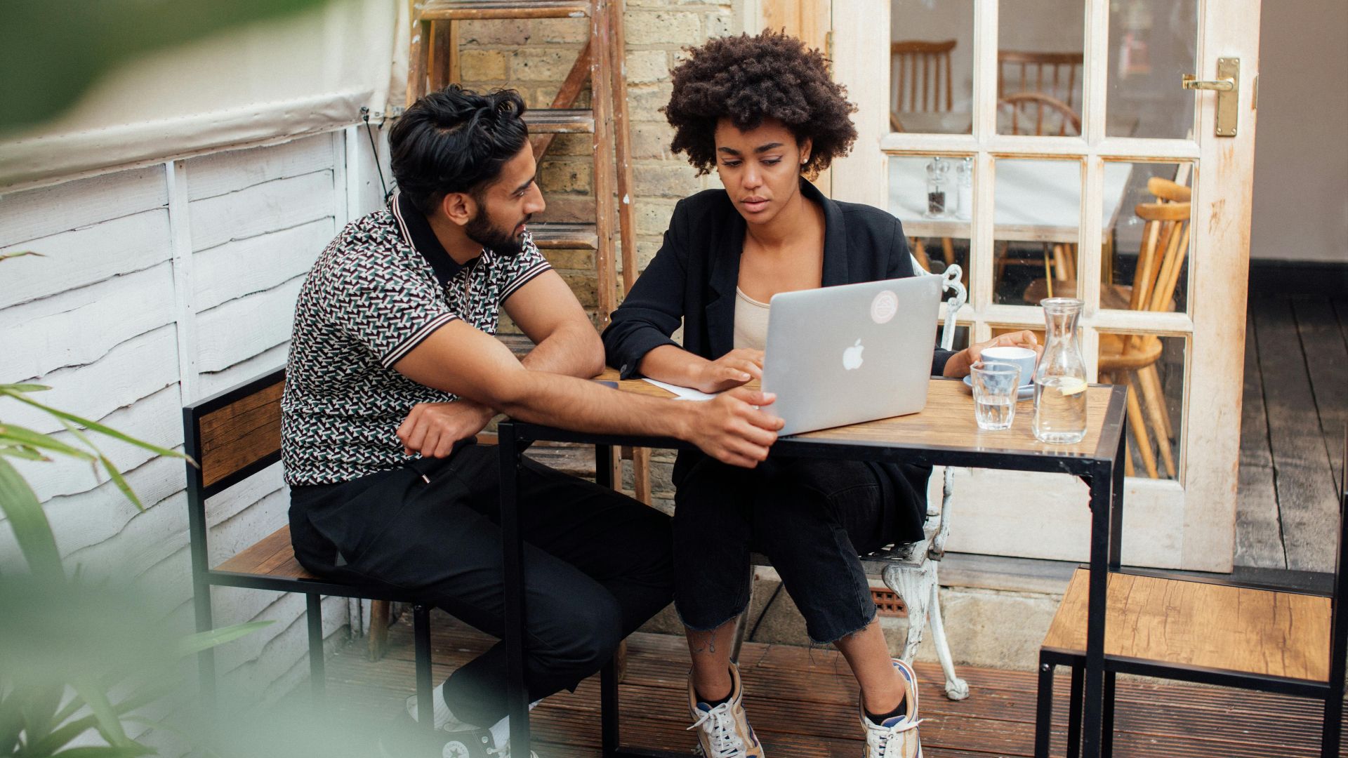 A man and woman working together on a laptop at an outdoor terrace.
