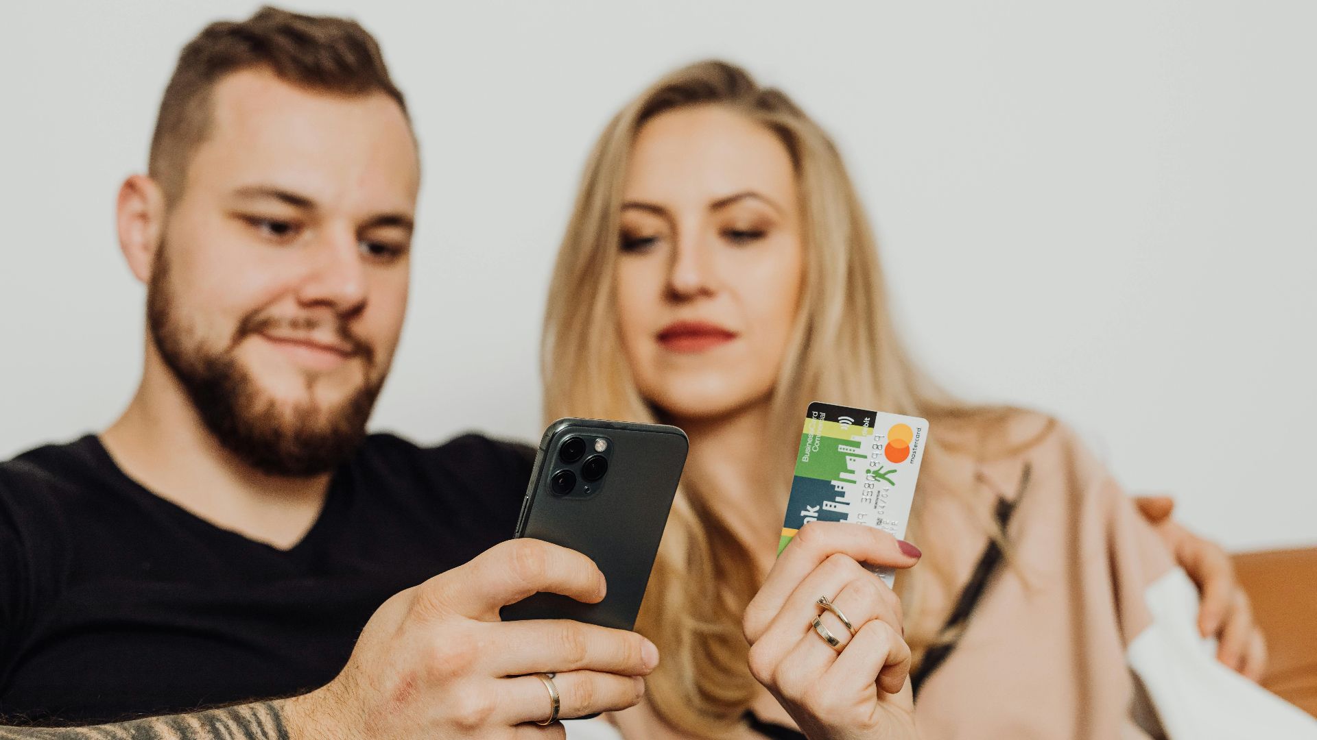 A couple shopping online together using a smartphone and credit card while sitting comfortably indoors.