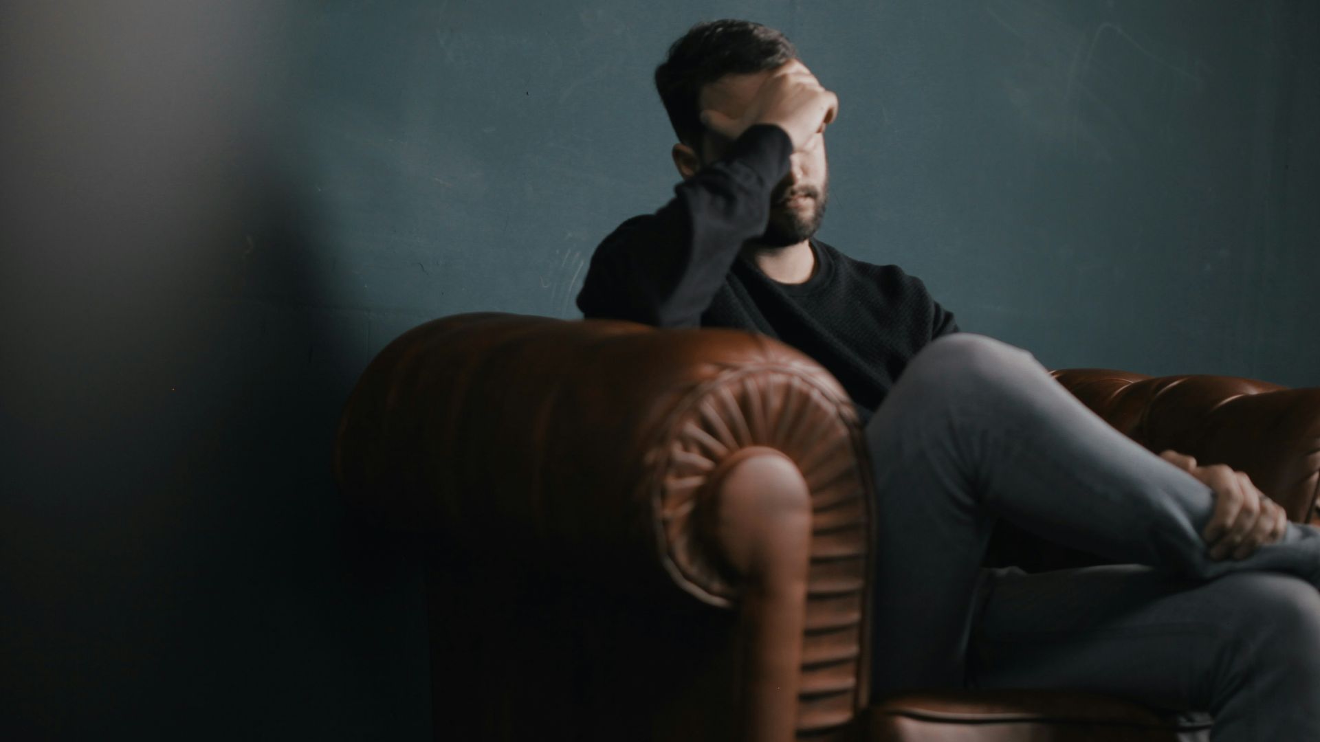 a man holds his head while sitting on a sofa