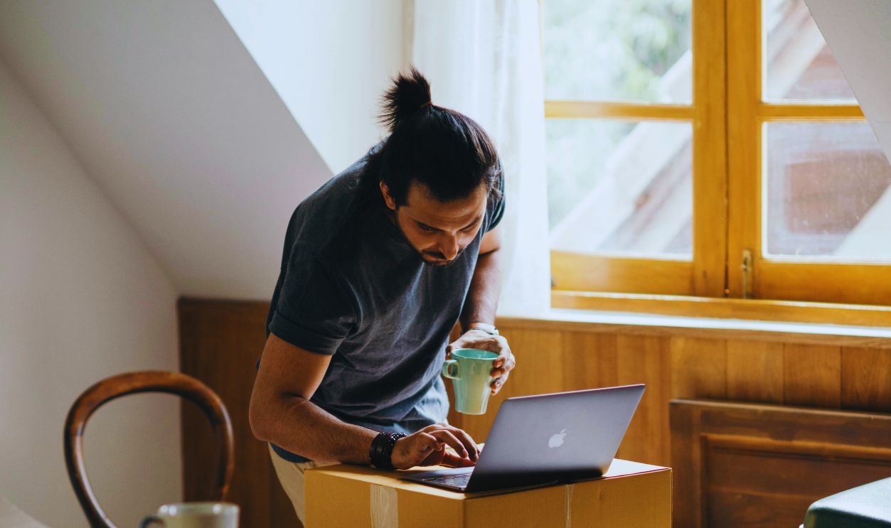 Ethnic man typing on laptop while preparing to relocate