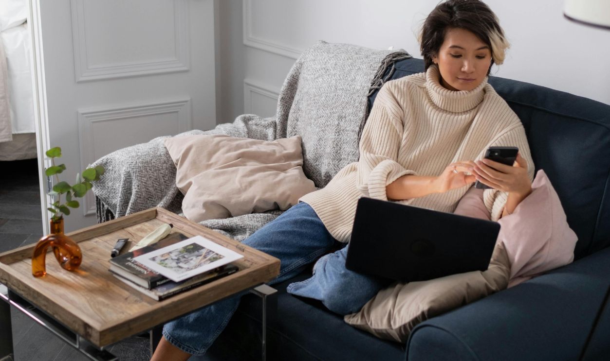 A Woman in a Sweater Using a Laptop and a Smartphone