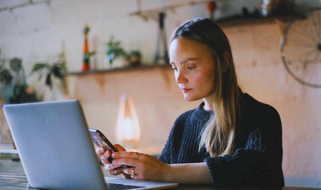 Serious woman browsing smartphone near laptop