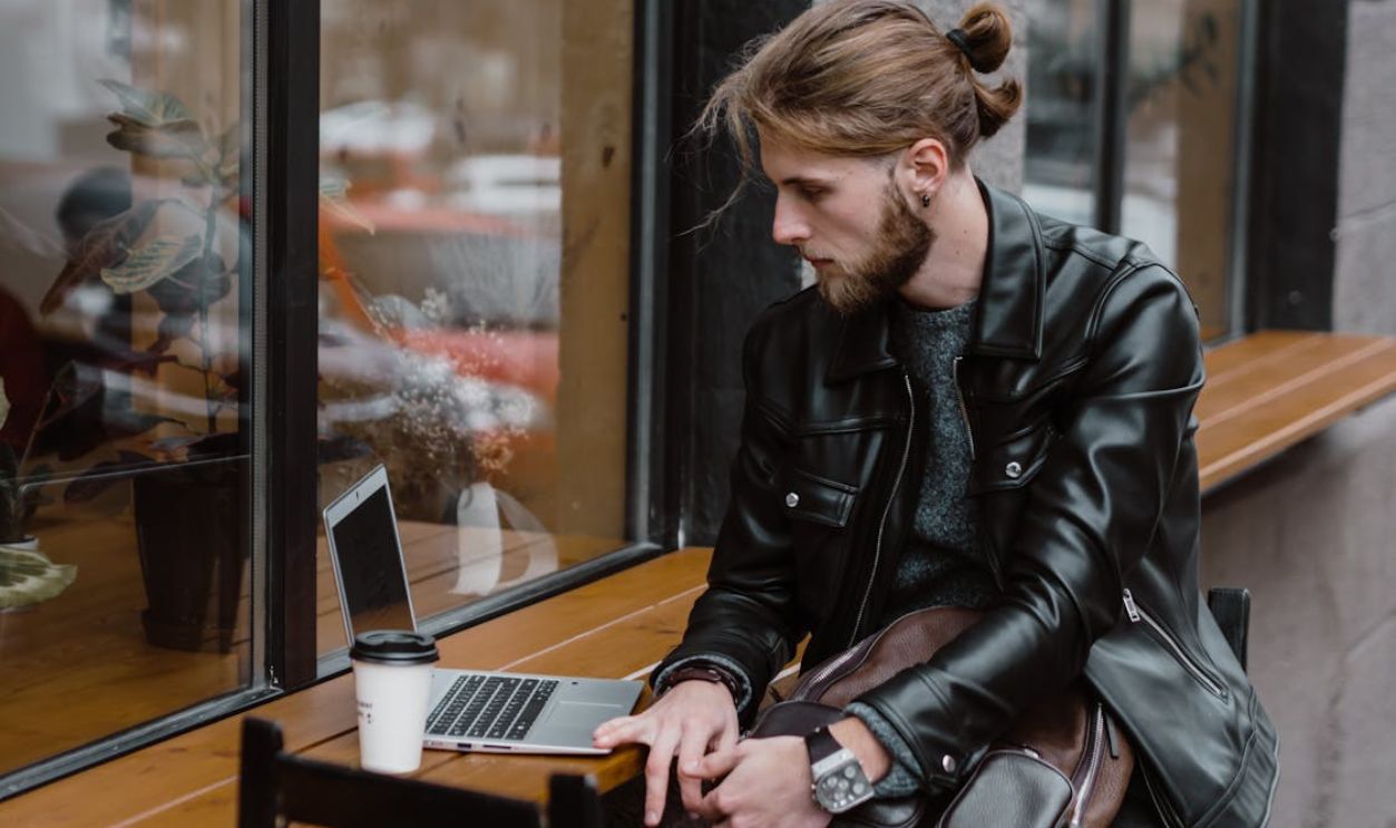 A Bearded Man Using a Laptop on a Wooden Table