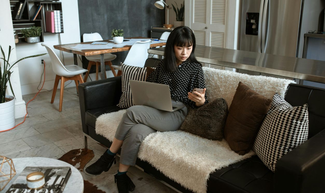 Woman Looking At Her Cellphone While Using Laptop