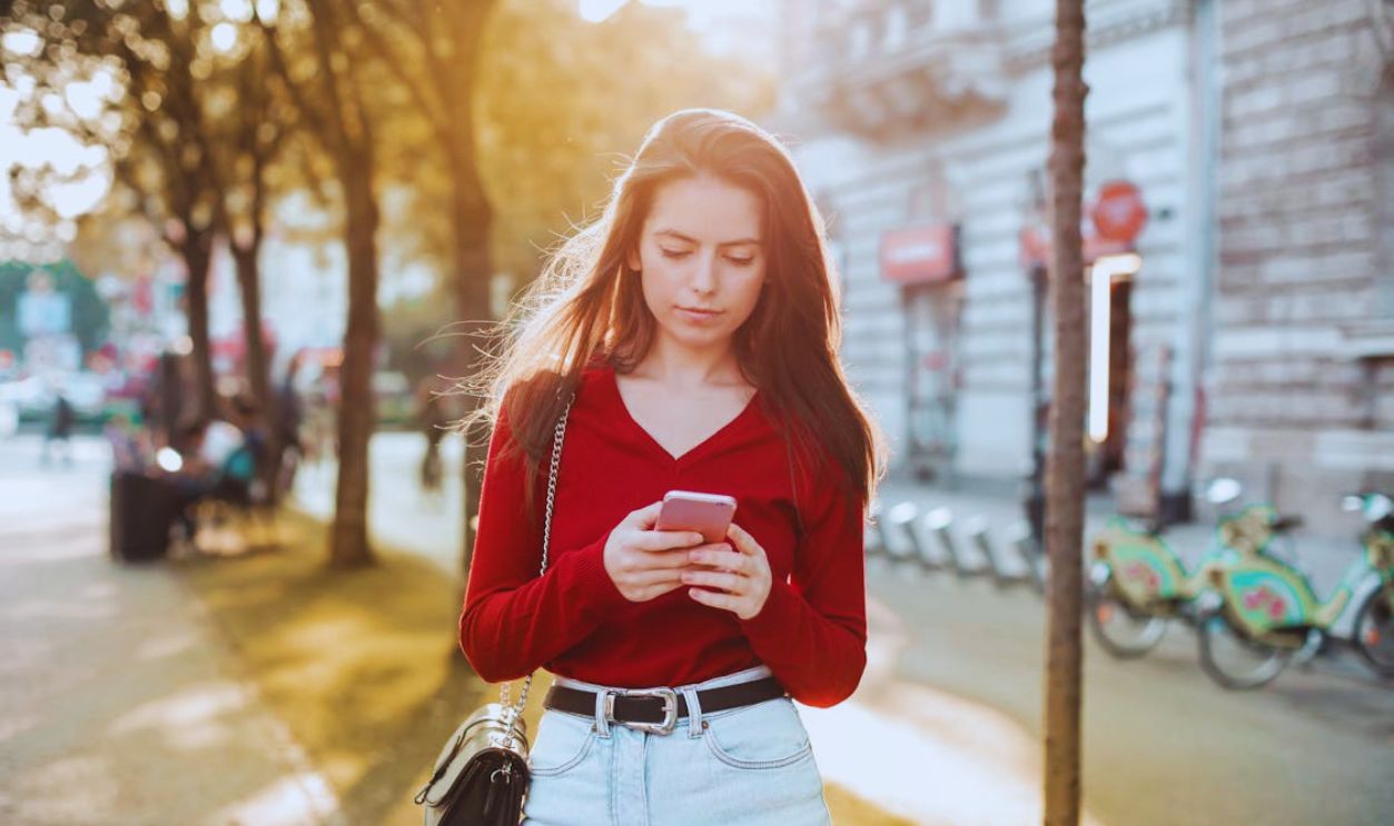 Woman in Red Long Sleeve Shirt and Blue Denim Jeans Looking at Her Cellphone