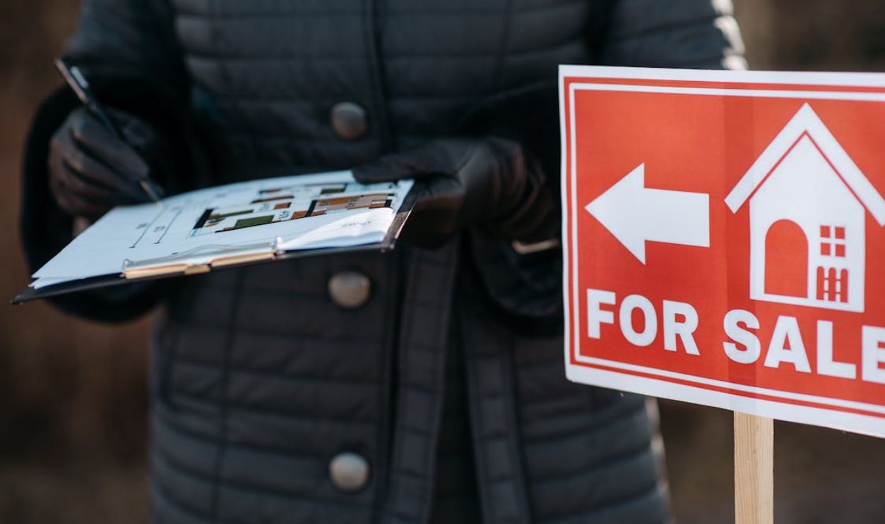 For Sale Banner and Person with Notepad Standing near