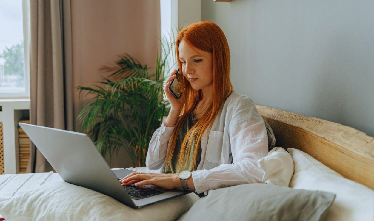 A Woman Typing on her Laptop and Talking on the Phone