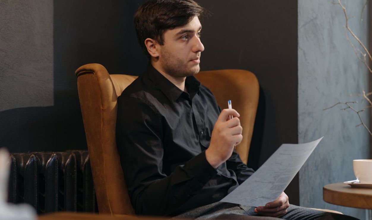 Man in Black Long Sleeve Shirt Sitting on a Chair While Holding a Paper