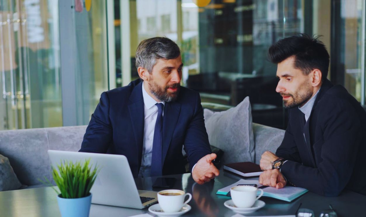 Two men in business attire sitting at a table with laptops