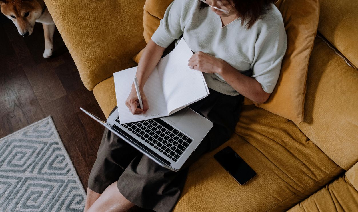 A Woman Writing While Using a Laptop