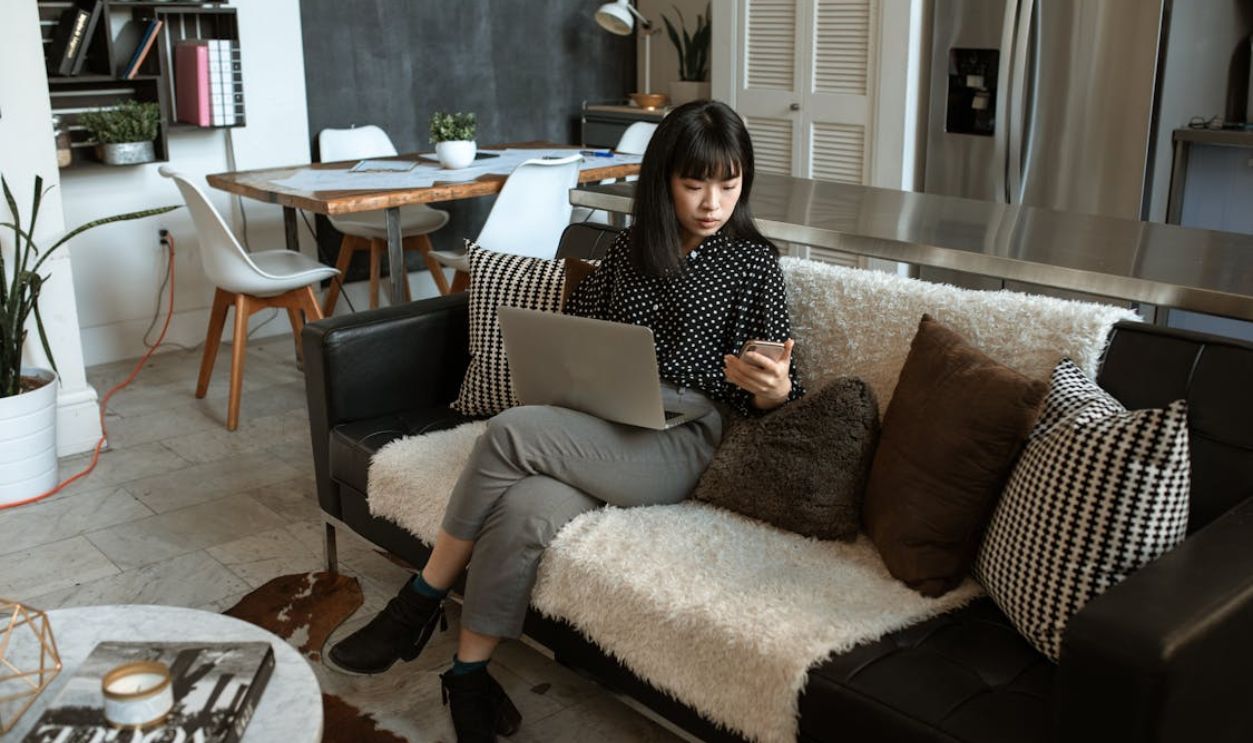 Woman Looking At Her Cellphone While Using Laptop