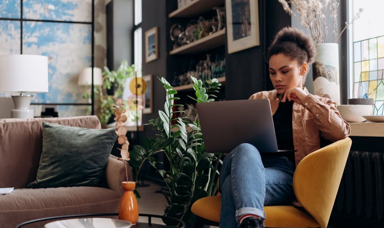 Woman in Brown Jacket Sitting on Armchair while Using Her Laptop