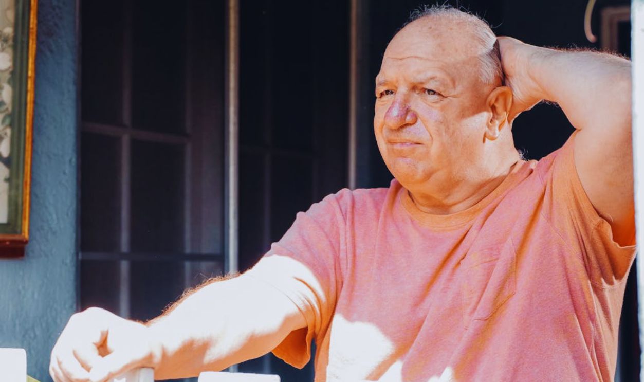 An Elderly Man Looking Outside with His Hand on His Head