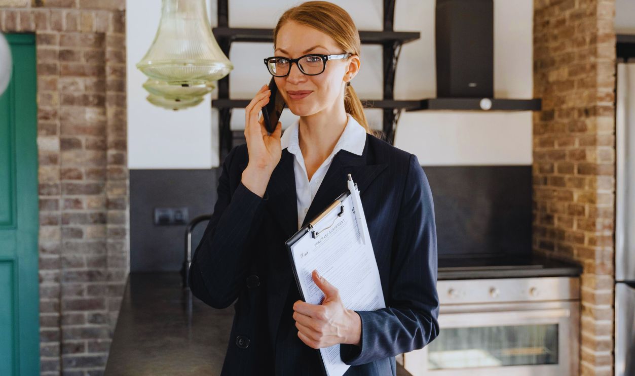 A Woman in Business Attire Holding Clipboard while Having Phone Call