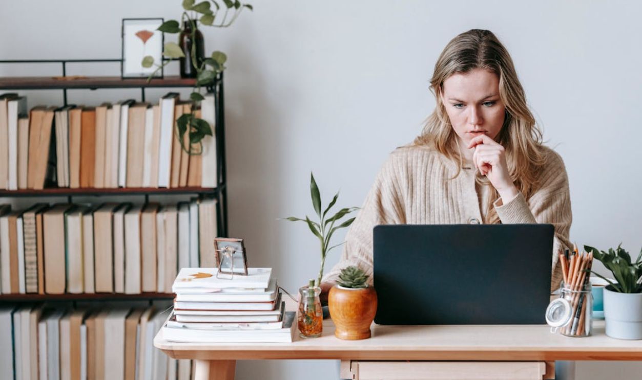 Pensive woman browsing laptop near books