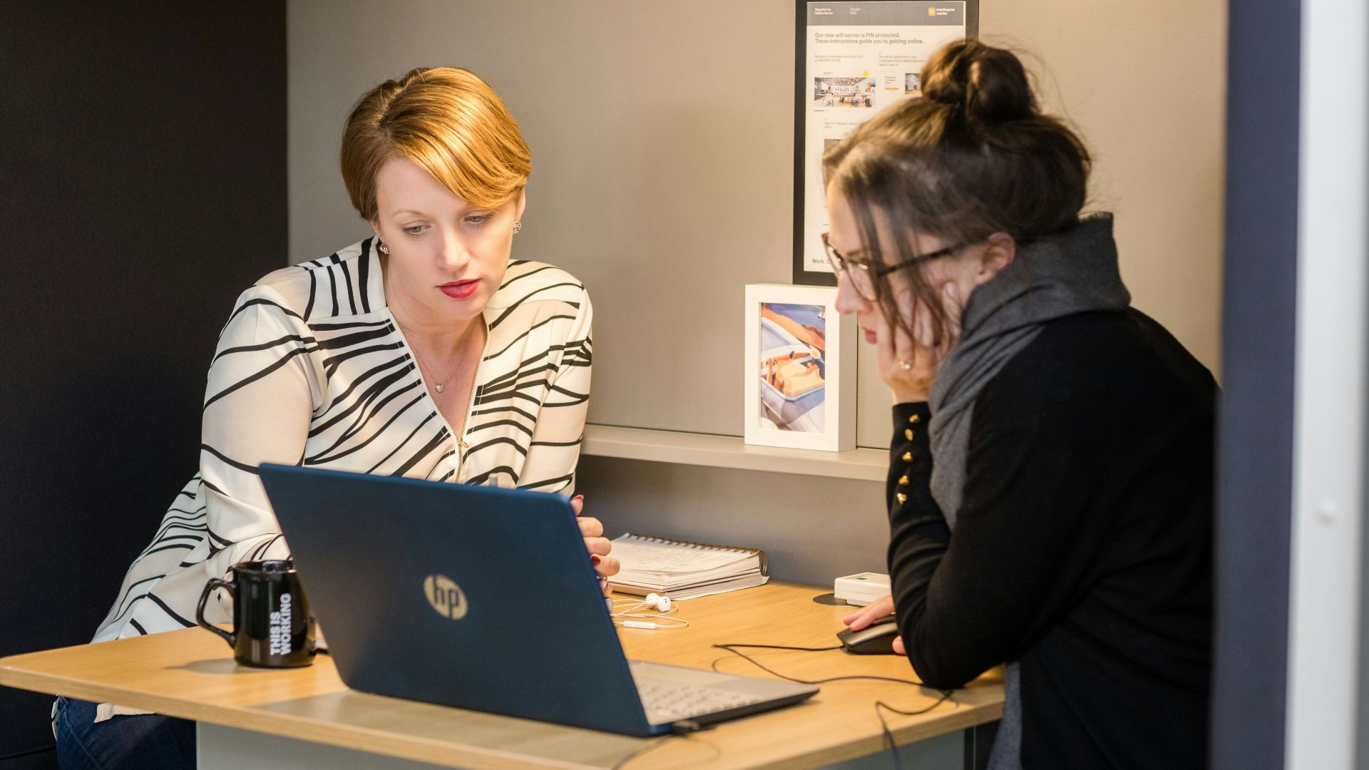 two women sitting at a table with a laptop