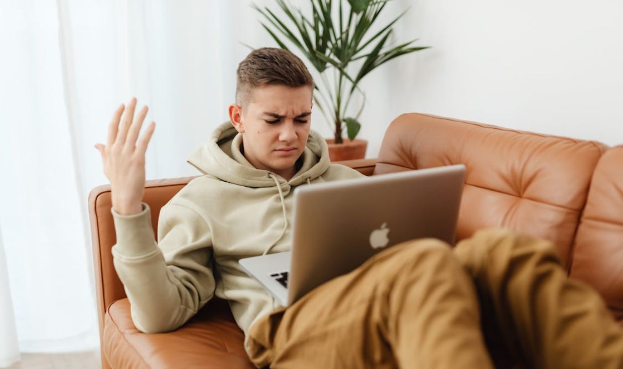 An Irritated Man Resting on a Couch while Looking at the Screen of His Laptop