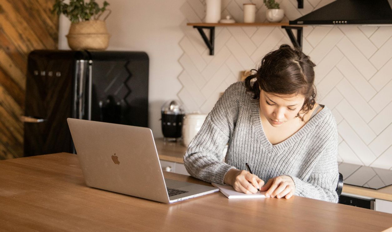 Focused female freelancer with laptop and notepad in kitchen
