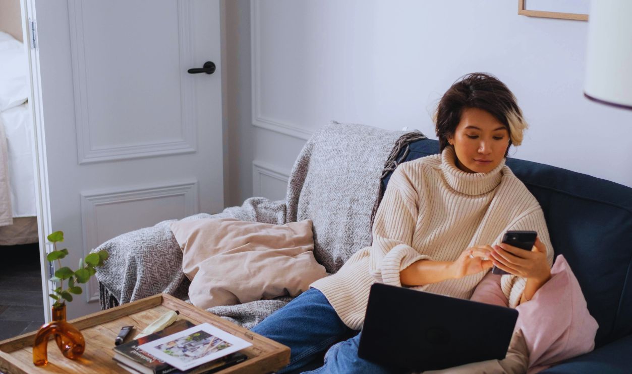 A Woman in a Sweater Using a Laptop and a Smartphone