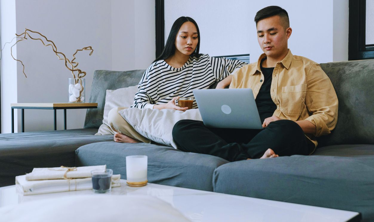 Man and a Woman Sitting on Sofa While Looking at the Screen of a Laptop