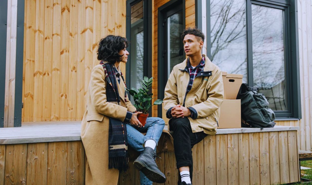 A Man and Woman Sitting Outside a Wooden House