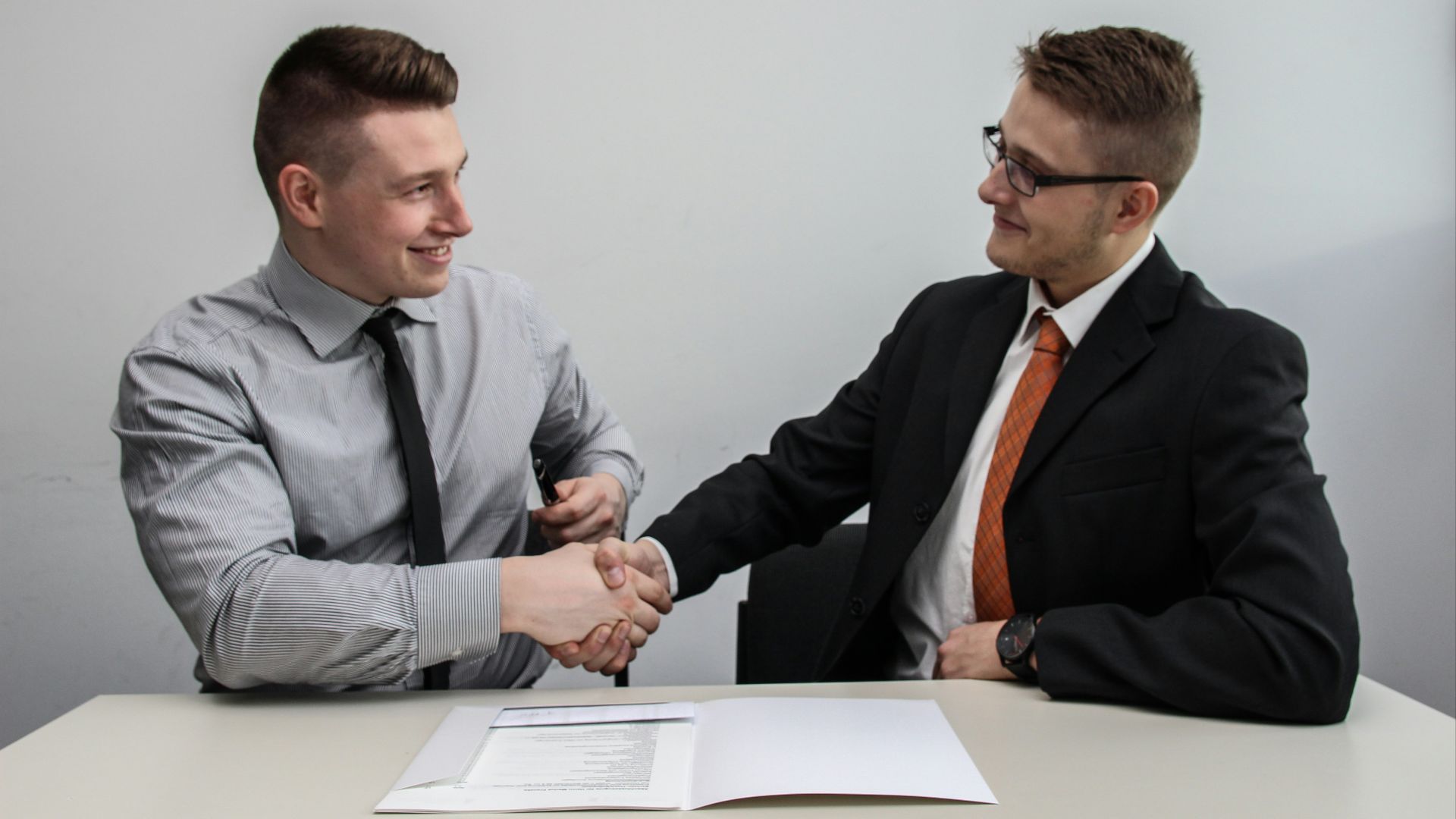 two men facing each other while shake hands and smiling