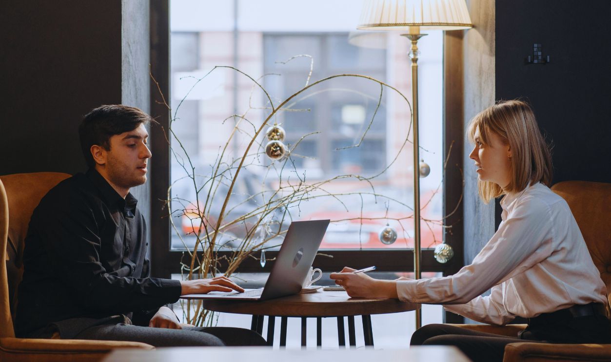 A Woman Sitting at a Table across a Man Using a Laptop