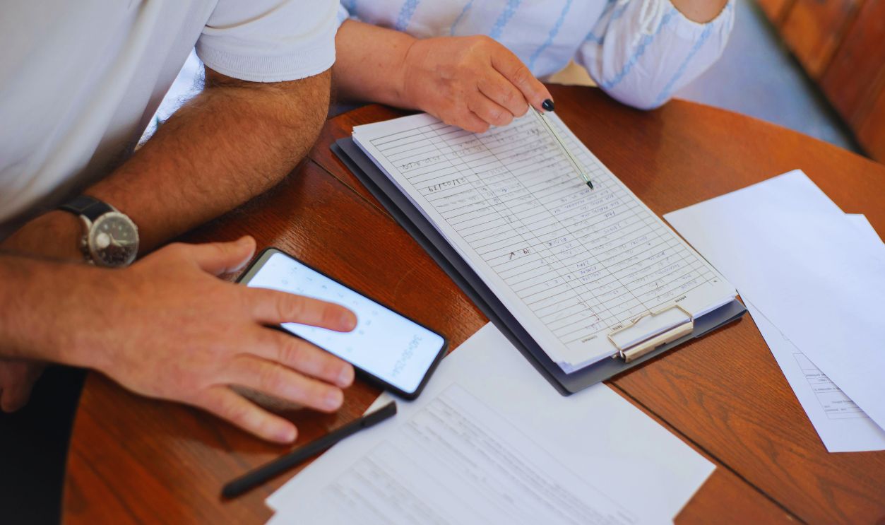 Close-up of Elderly Man and Woman Sitting at the Table with Documents and Using a Smartphone