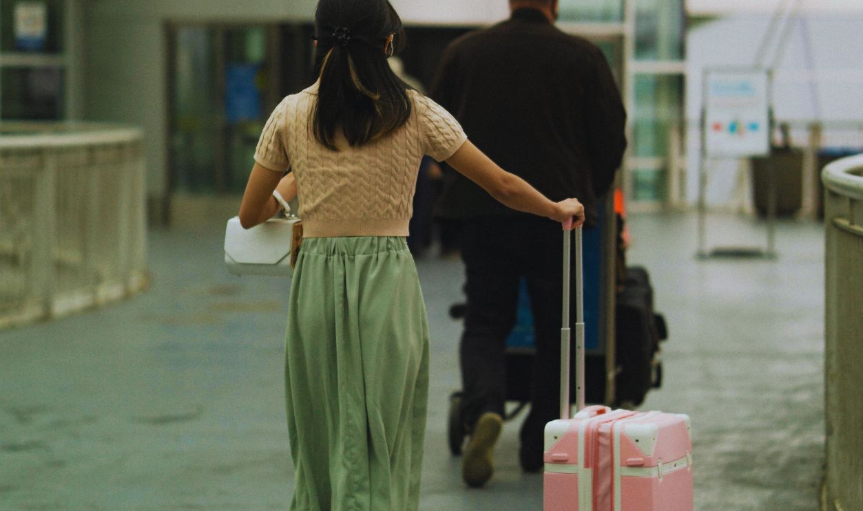 Woman in Brown T Shirt Pushing Her Pink Luggage and Man in Black Long Sleeves Pushing Trolley