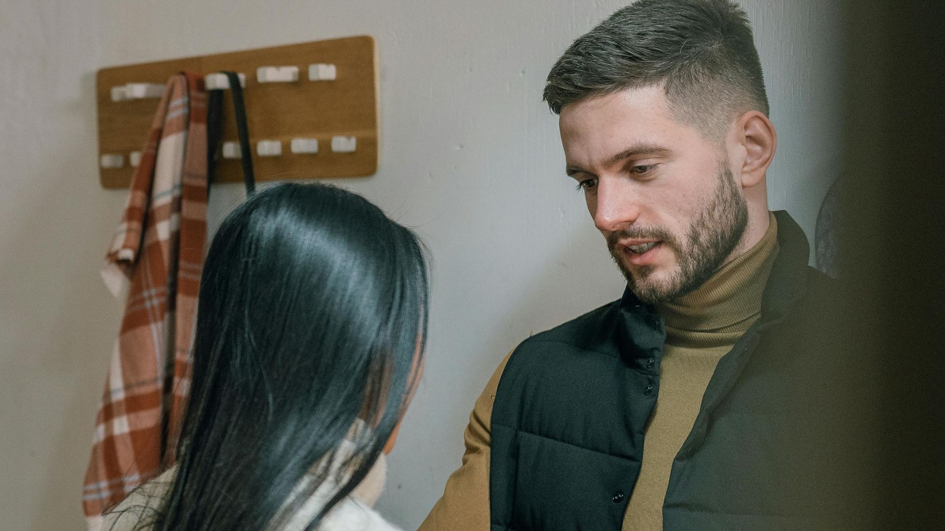 A man and woman talk inside a cozy home. They appear engaged in a conversation.