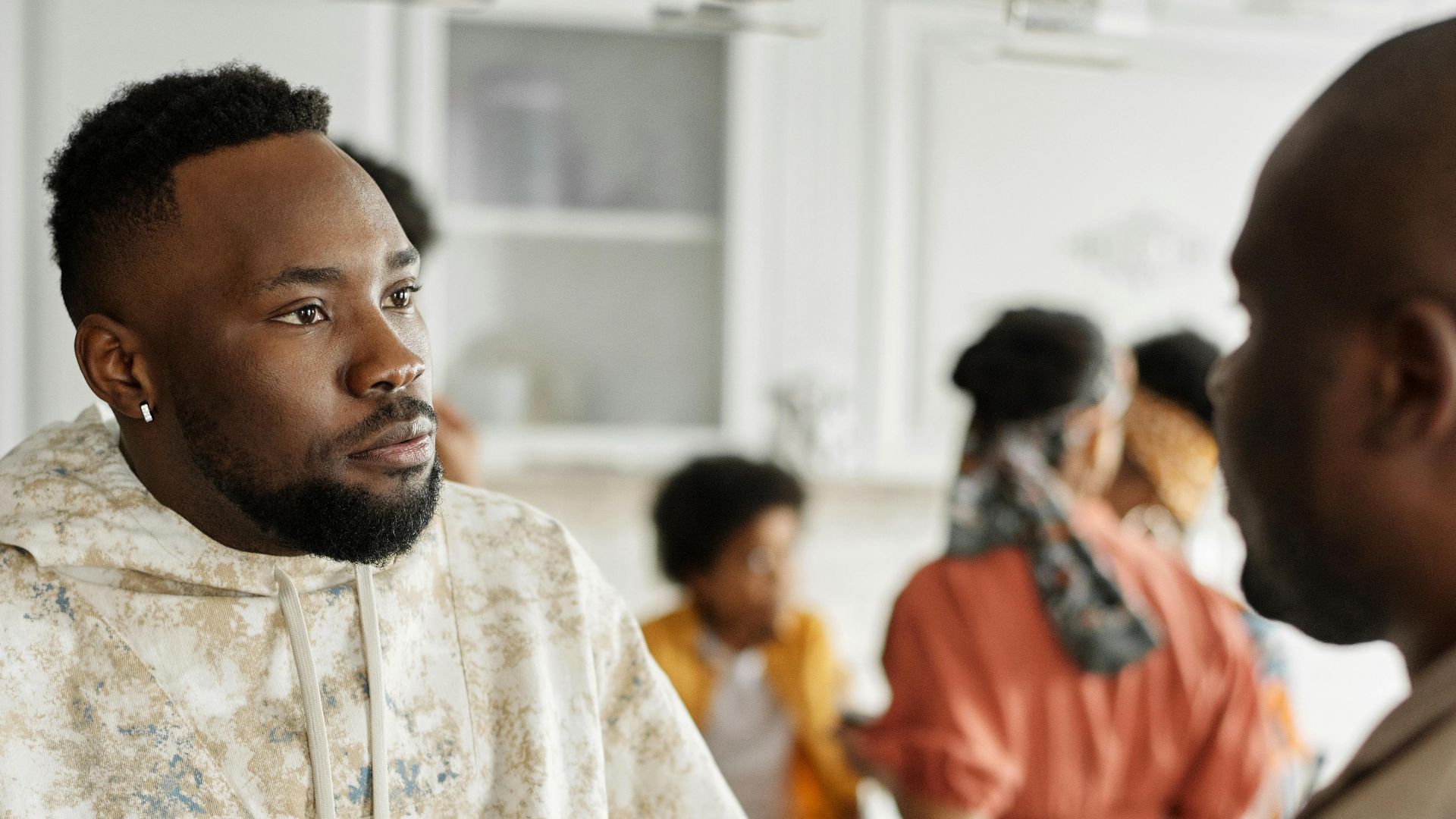 Two friends having a discussion at a casual indoor gathering with others in the background.