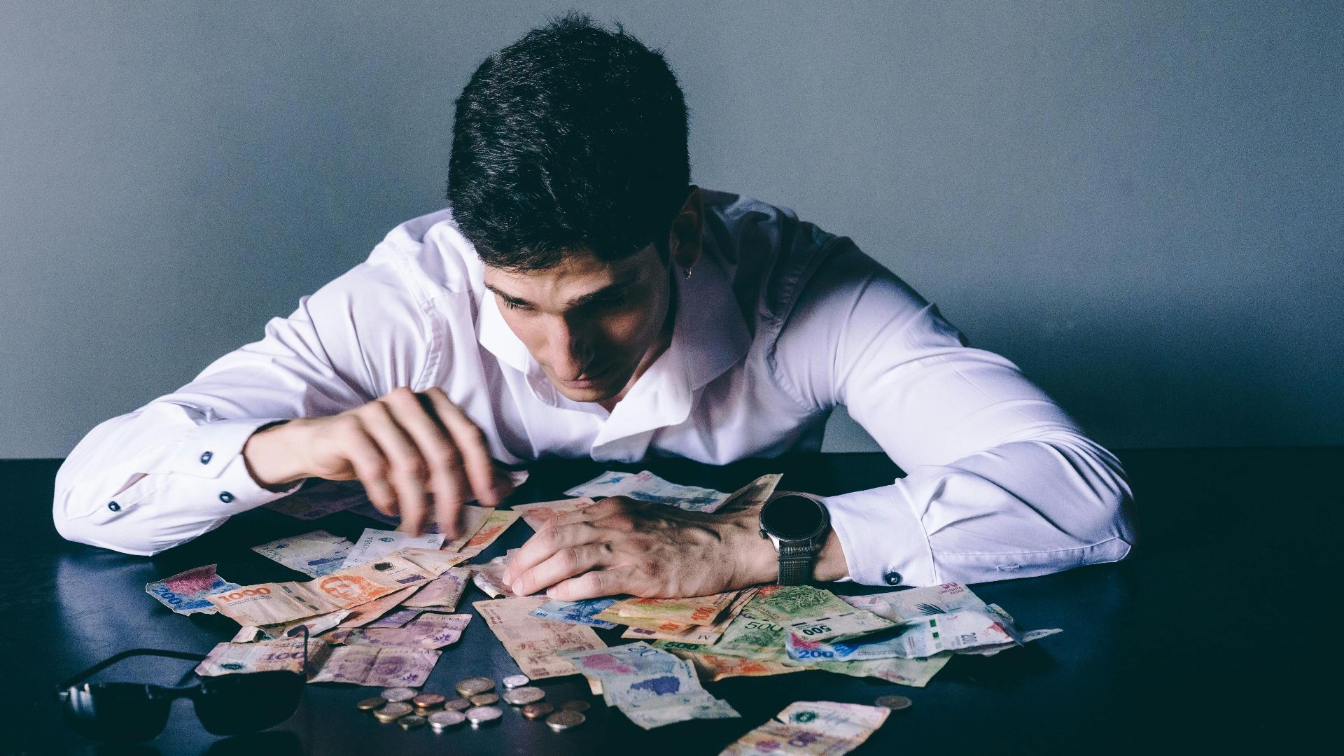 Focused man counts various international currencies on a dark desk indoors.