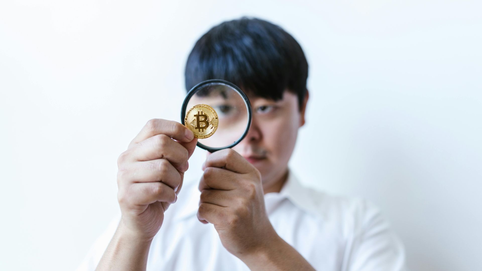 Close-up of a man examining a Bitcoin coin with a magnifying glass, symbolizing cryptocurrency analysis.