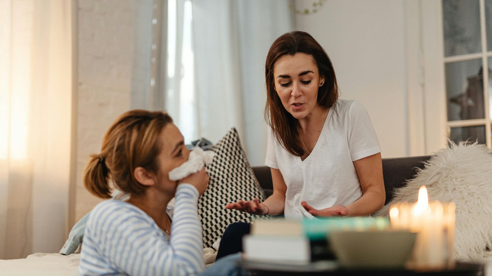Two women engage in a heartfelt conversation, indoors, with candles creating a cozy atmosphere.