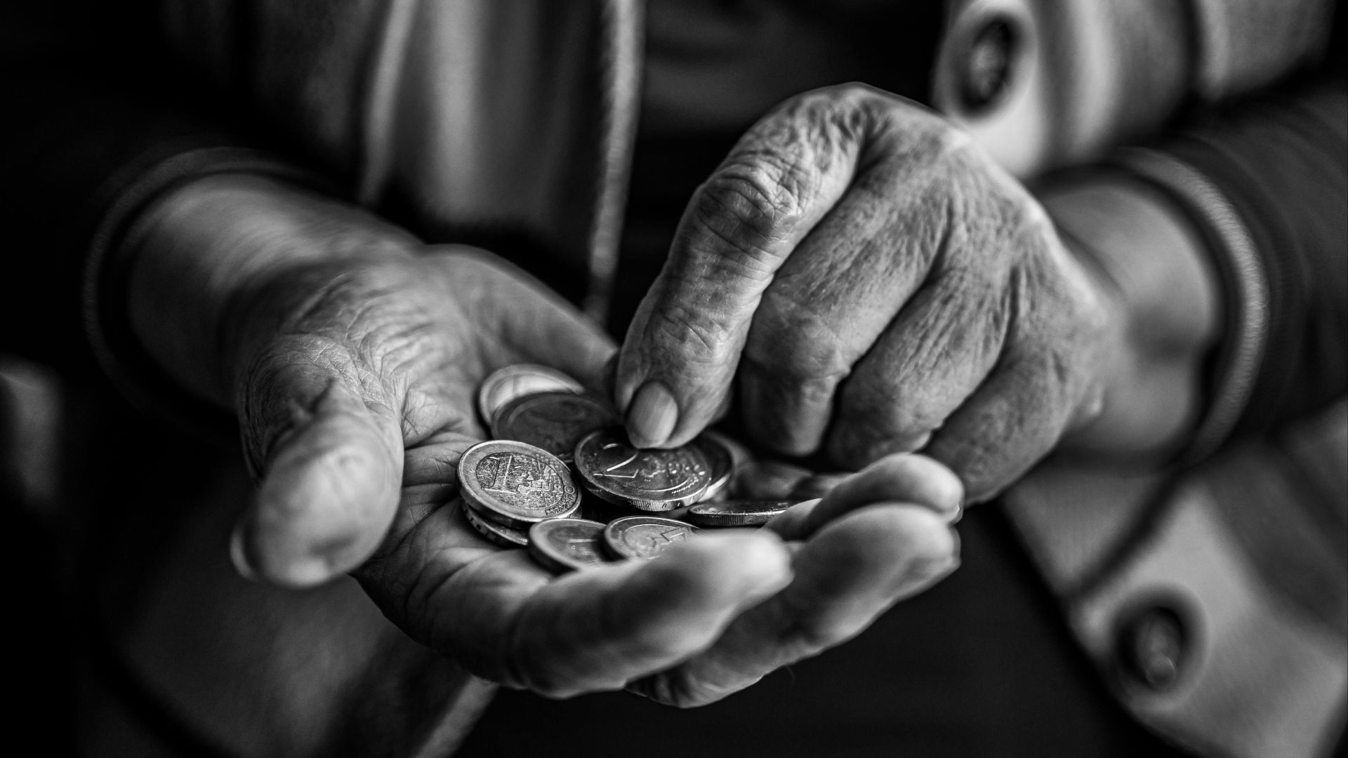Close-up of elderly hands holding and counting coins, captured in black and white for a timeless feel.