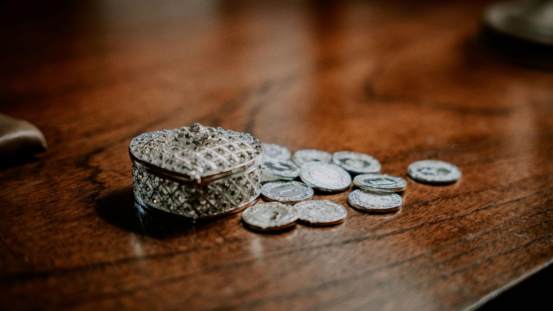 Close-up of a decorative heart-shaped box with scattered coins on a wooden surface.