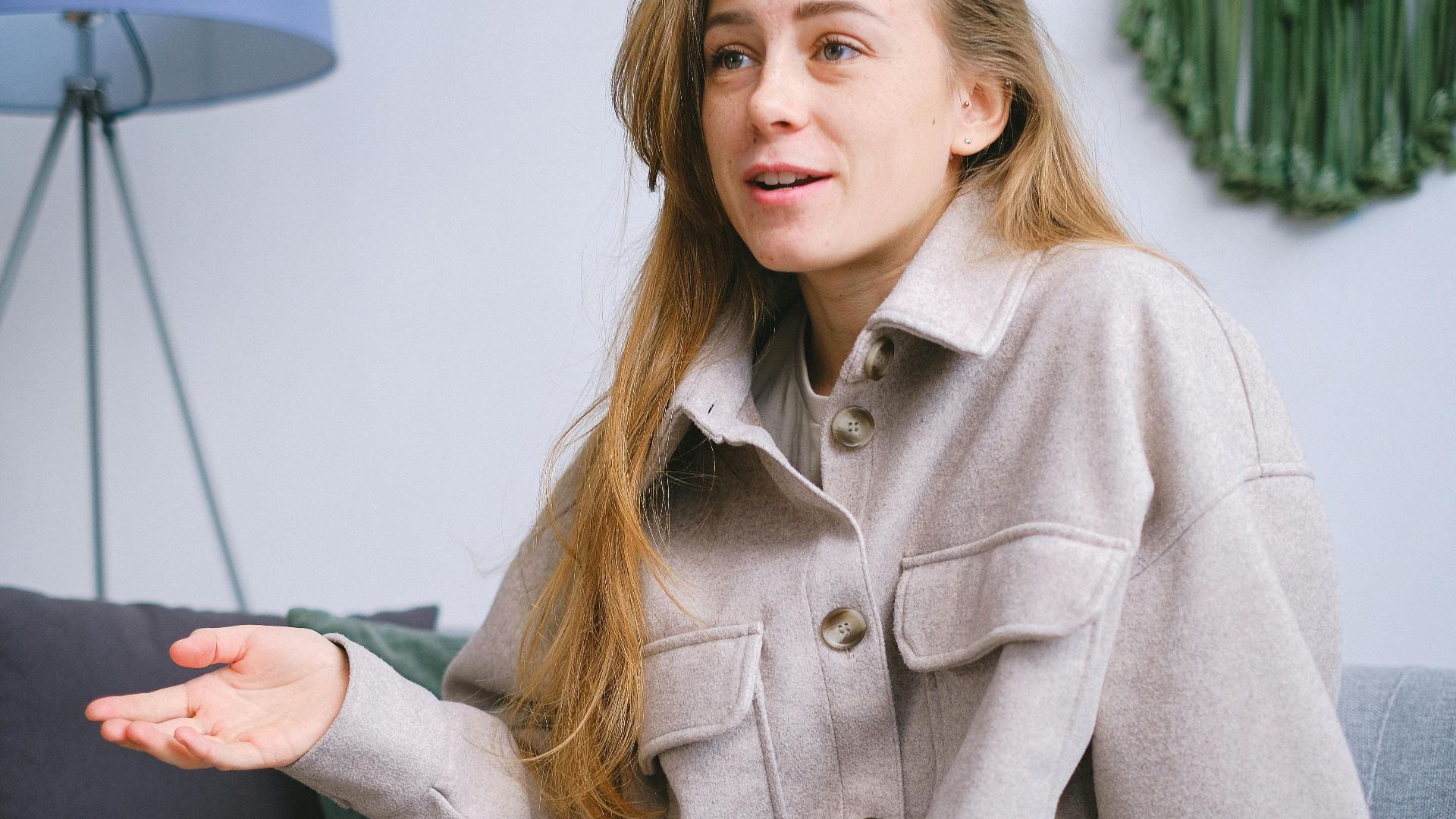 Crop female with long hair in elegant clothes sitting on comfortable sofa while talking in light room during psychotherapy session