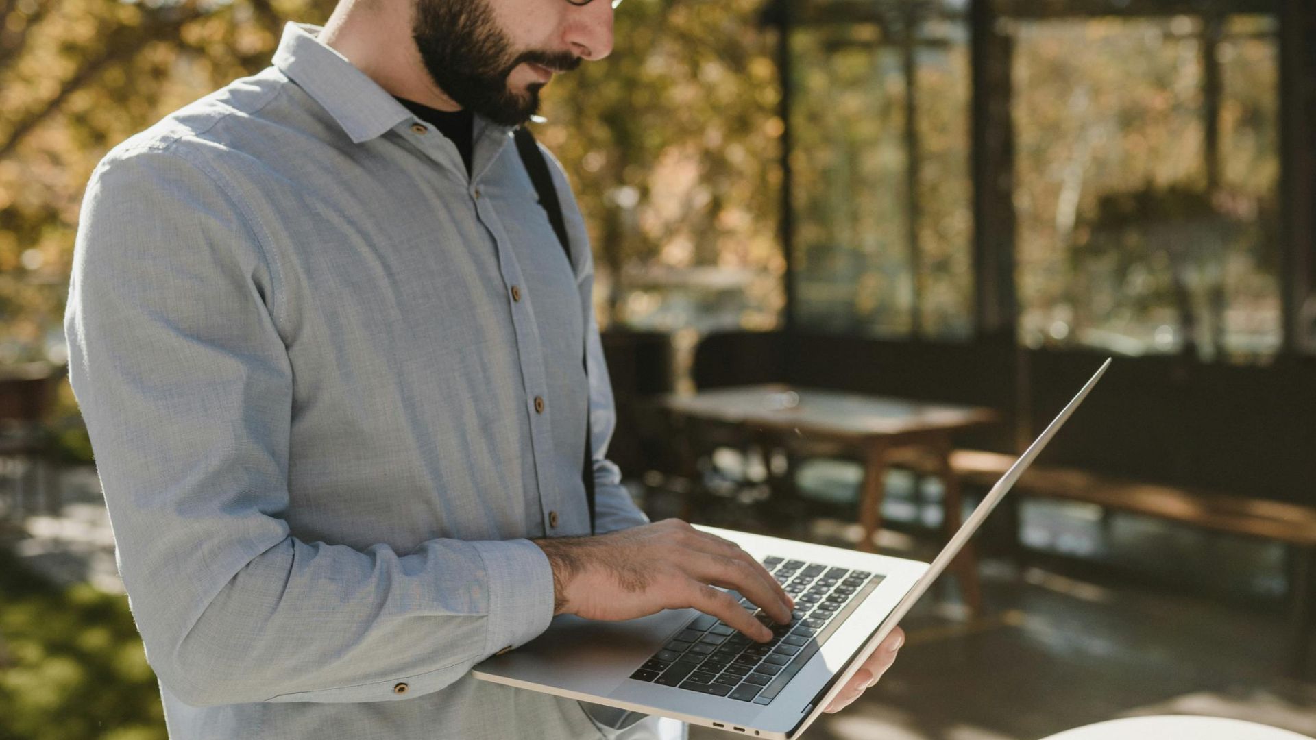 A bearded man using a laptop outside under string lights, showcasing remote work lifestyle.