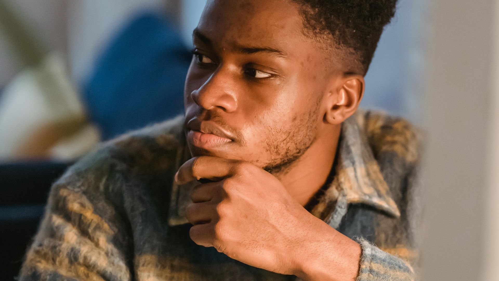 Serious young African American male freelancer thoughtfully looking away and touching chin while working on computer