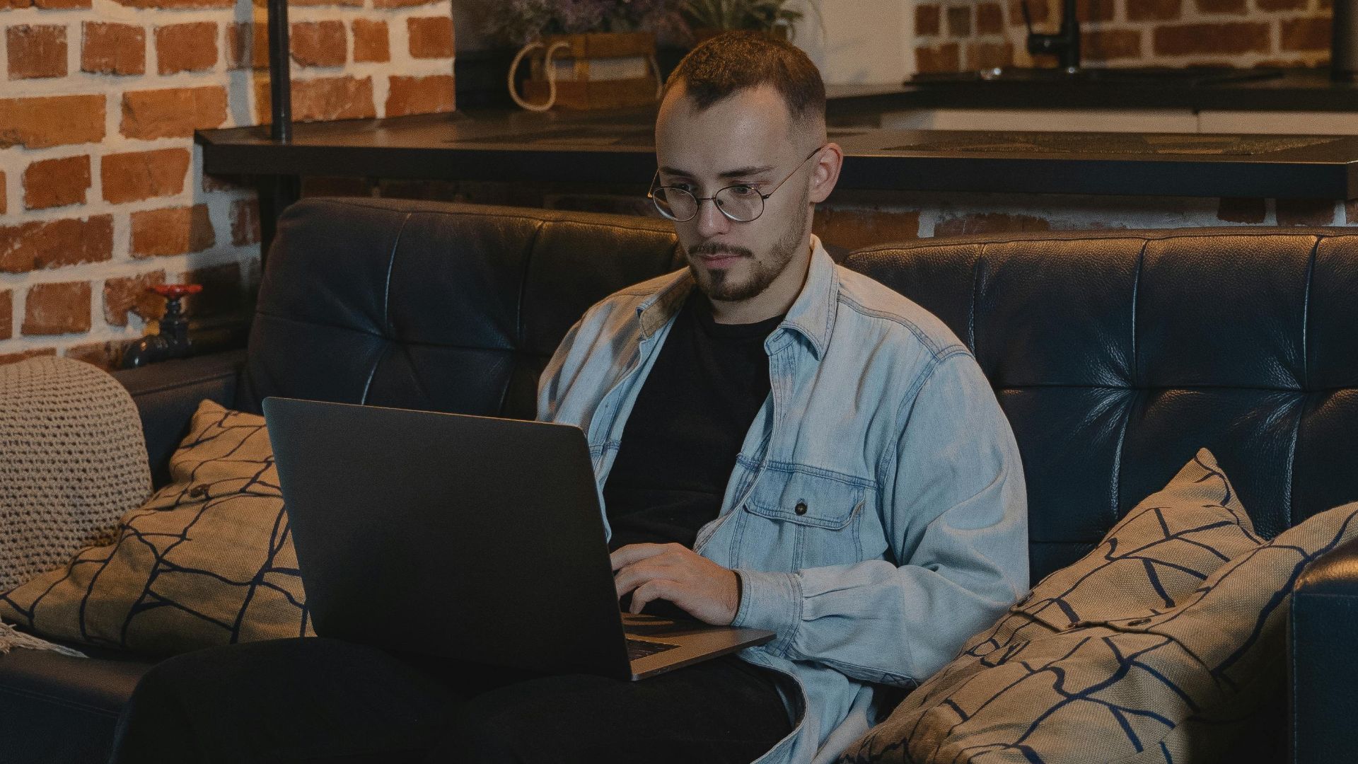 A bearded man sits comfortably on a couch, working on his laptop in a stylish living room.