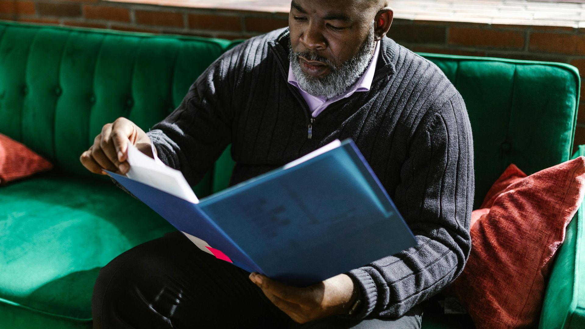 African American adult man reviewing documents on a green sofa, indoors.