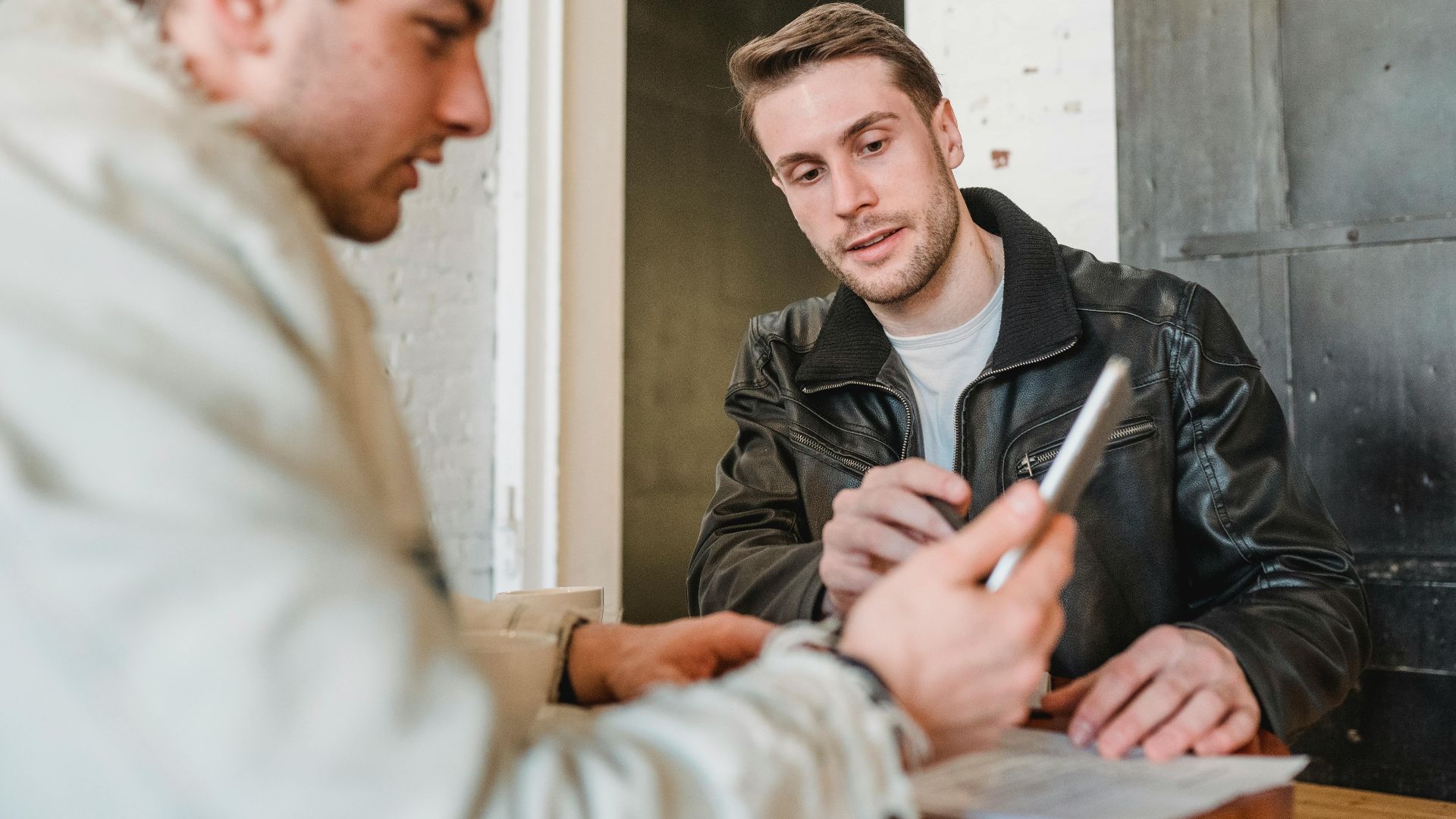 Two men engaged in a business discussion at a cafe, using a tablet and paper notes.