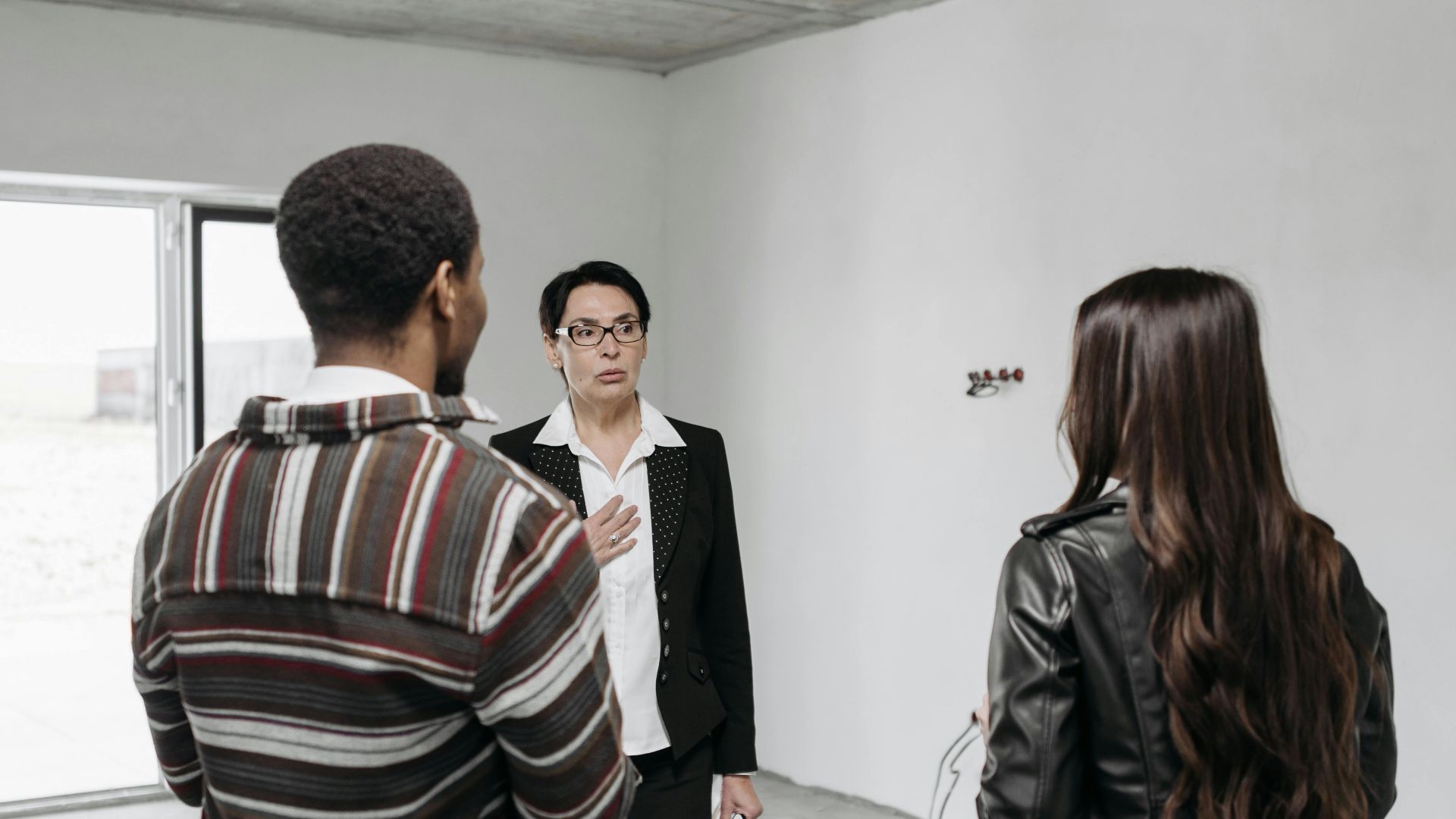 Realtor showing young couple a house, discussing details inside a modern, unfurnished space.