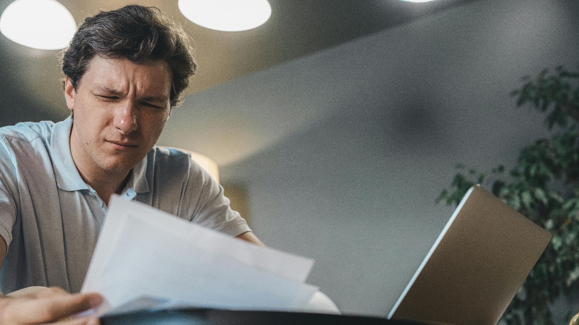 Man focusing intently while reviewing documents at a desk with a laptop.