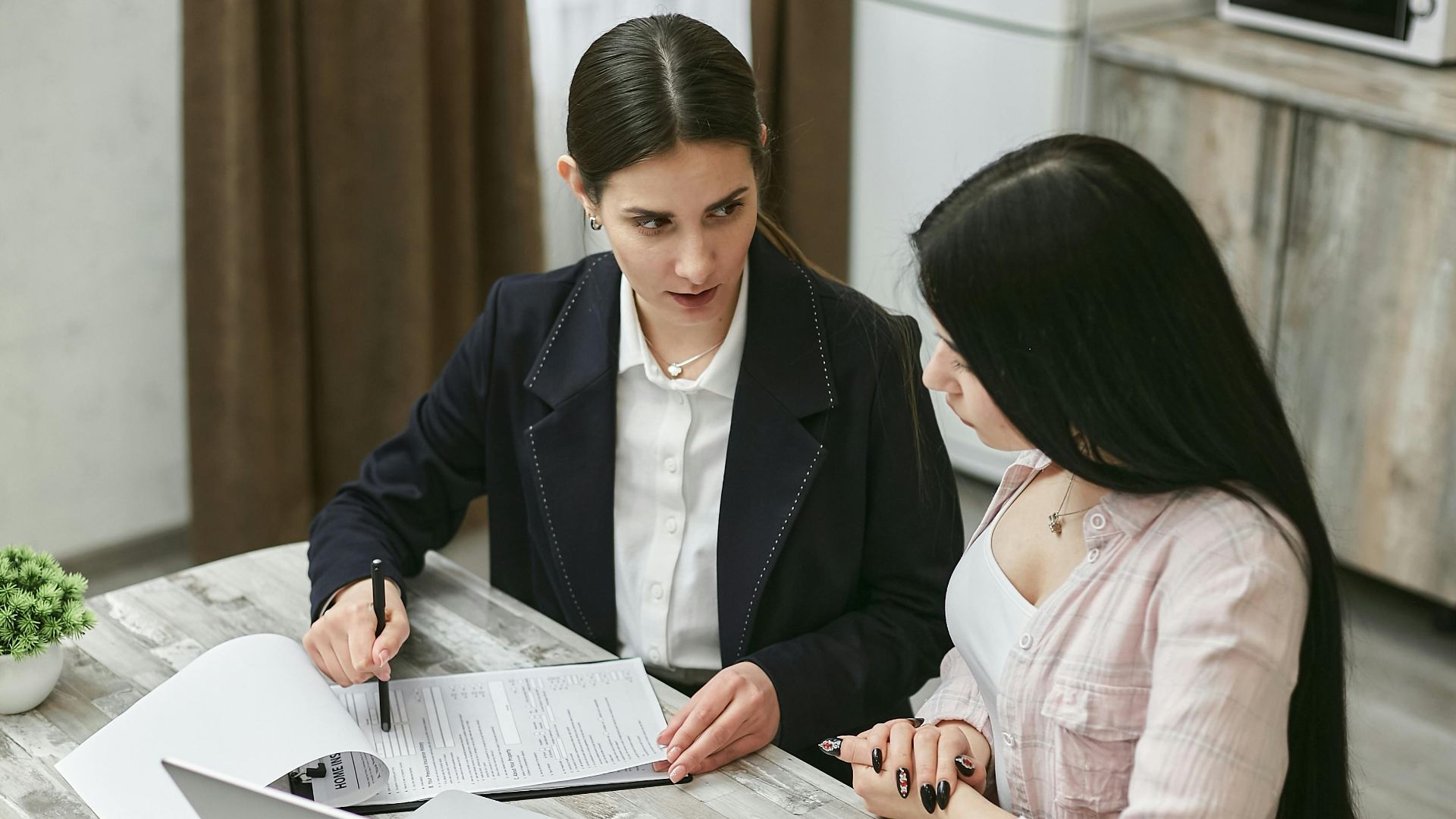 Two businesswomen engaged in a contract discussion at an office table.