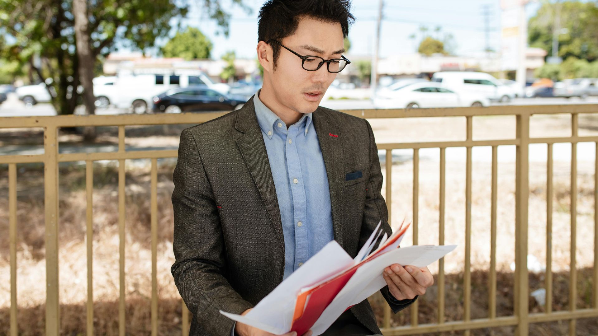 Asian businessman in a suit checking documents outdoors on a sunny day.
