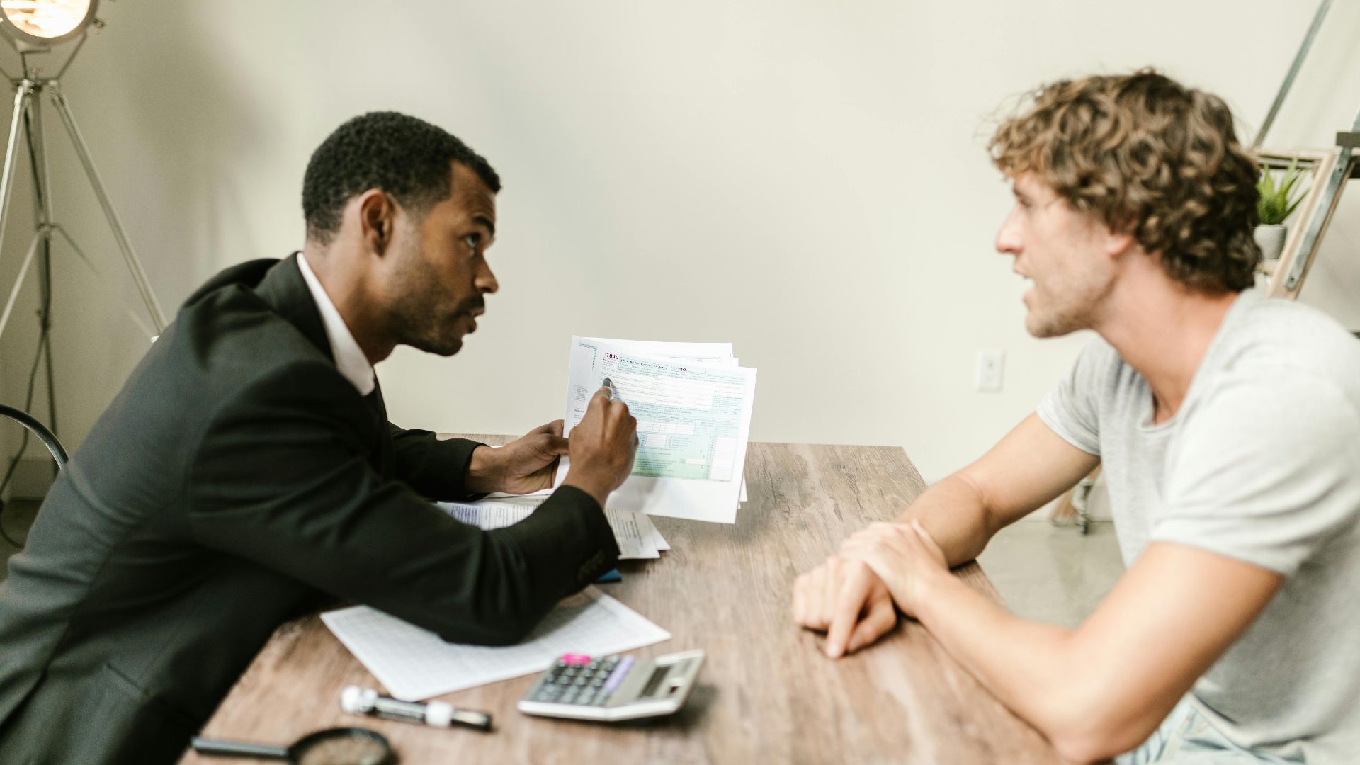 A financial advisor discusses paperwork with a client at a desk in a modern office.