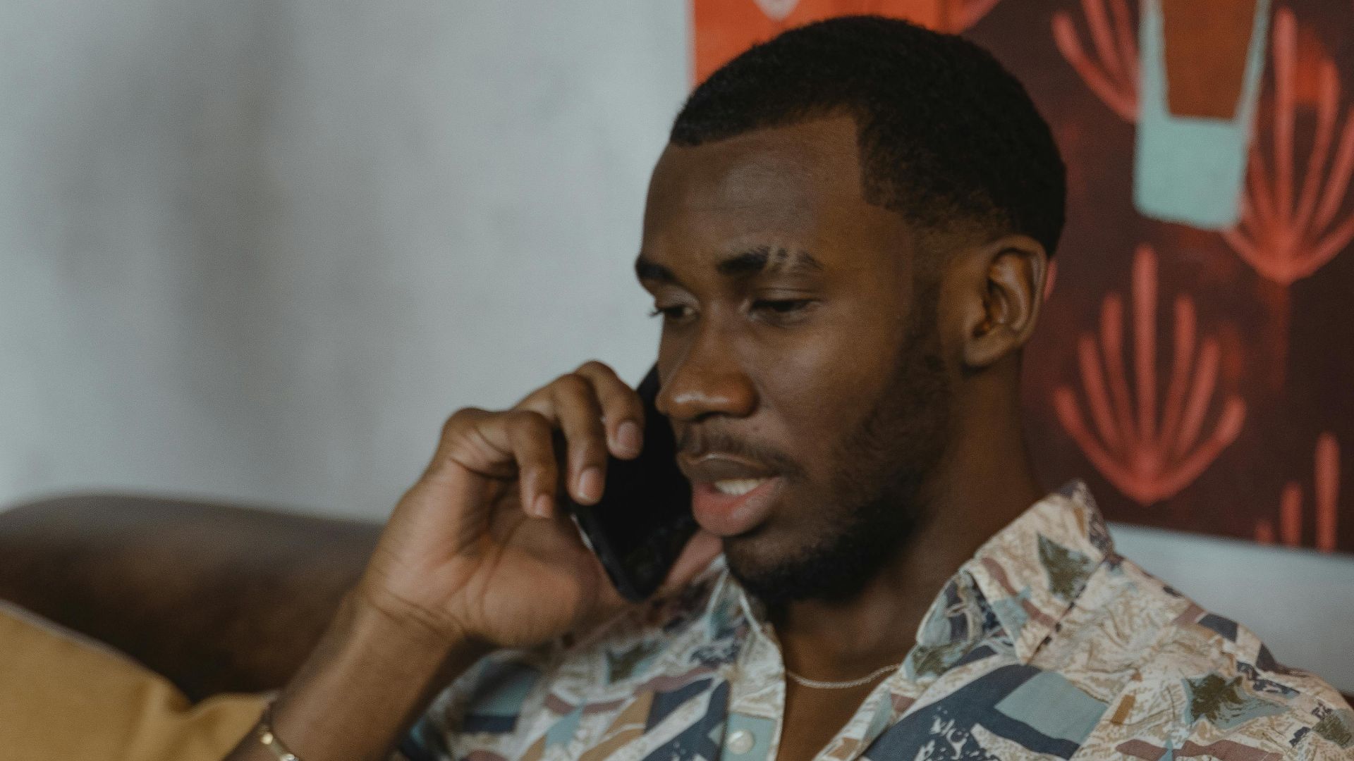 Stylish man talking on the phone while working from home on a laptop.