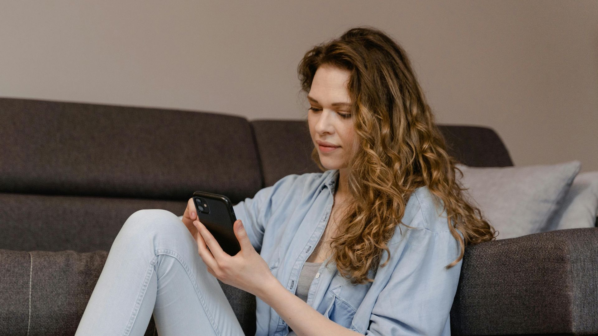 Brunette woman sitting on the floor, using smartphone, enjoying leisure time.