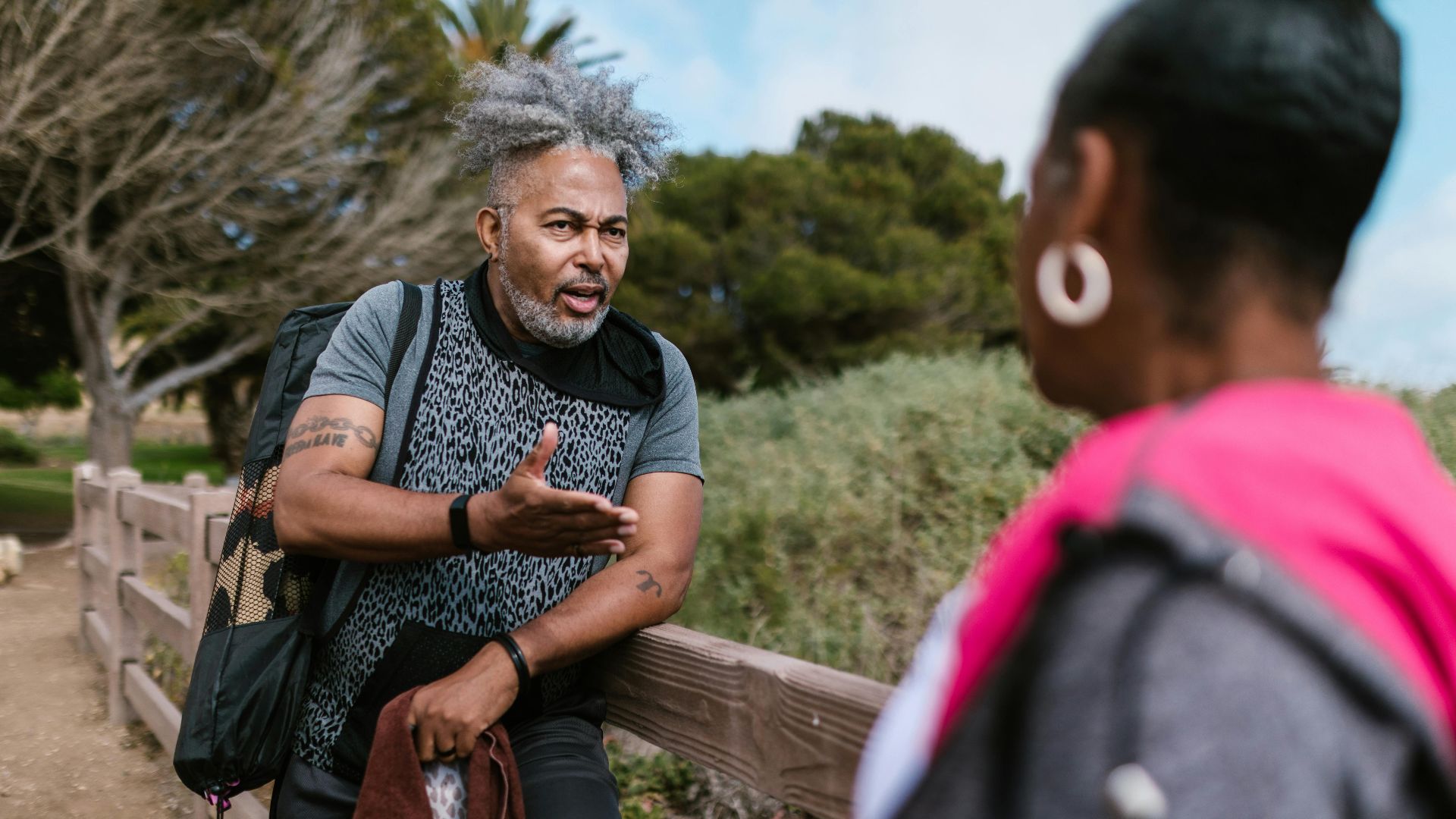 Two adults engage in a lively conversation outdoors by a wooden railing.